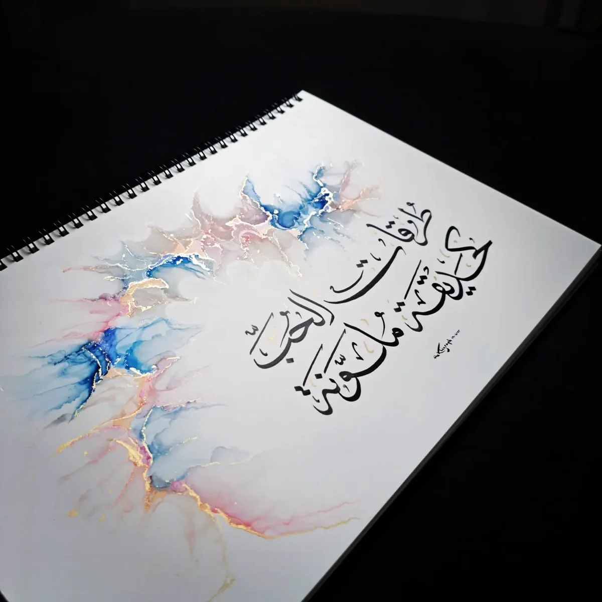 Arabic calligraphy over a cloud of pink, blue and gold ink